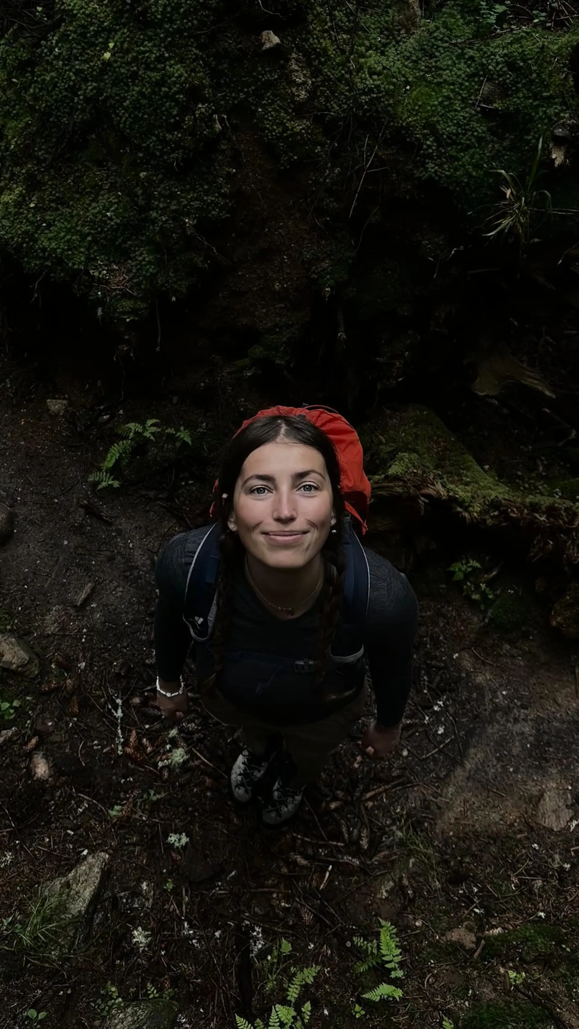 Kristína Turčanová looking up, in a mossy forest with her pack